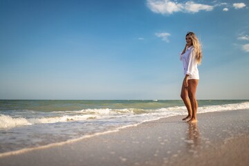 A tanned girl in a blue swimsuit and a light shirt enjoys the summer at the seaside