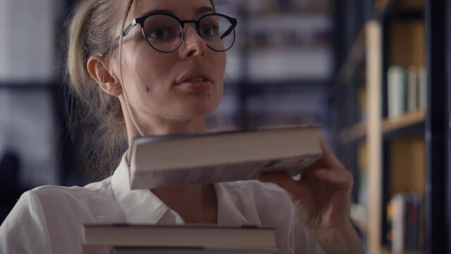 Sexy woman holding pile of books in the library, putting more on the stack