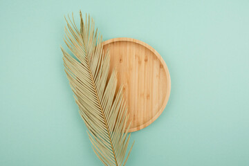 Wooden plate for product presentation with palm leaf. Mockup background with podium and copy space. Empty cylindrical platform for cosmetic. Top view on light mint green background. Skincare cosmetic.