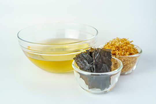 Dashi or Japanese soup stock in the glass bowl with the ingredients for cooked dashi such as kombu and katsuobushi (Japanese seaweed and dried smoked skipjack tuna) isolated on white background.
