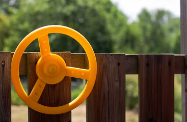 Close up of a yellow plastic wheel on wooden Jungle Gym for numerous adventures, swing set and outdoor playhouse, backyard playset with slide for kids as a playground activity for endless fun and play