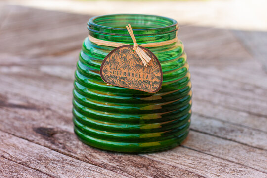 Scented green citronella glass candle holder used as a mosquito repellent standing on a wooden table top. Lemongrass green candles to prevent mosquitoes prick and to keep them away on a summer evening