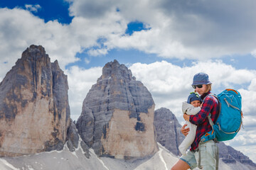Fototapeta na wymiar Young mom with baby boy travelling with backpack. Mother on hiking adventure with child, family trip in mountains. Vacations journey with infant National Park Tre Cime di Lavaredo, Dolomites, Italy