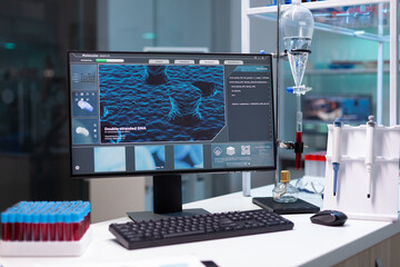 Close up of monitor with scientific dna illustration in empty laboratory. Nobody in microbiology cabinet with professional tools, micro pipette, tray of vacutainers and computer.