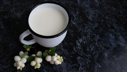 White enameled mug with milk and white snowberry berries on a dark gray background