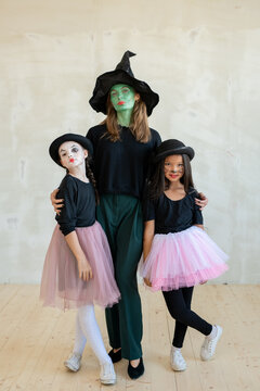 Young witch with her face painted green embracing two girls in pink skirts