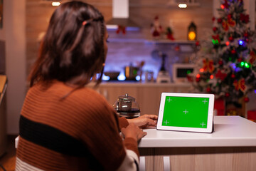 Caucasian adult watching green screen technology on tablet sitting at kitchen counter. Young woman...