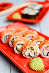 California sushi rolls served on a red plate over light wooden background. Close up, selective focus on sushi.