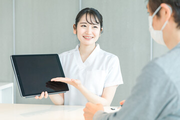 タブレットPCで受付する白衣の女性と患者
