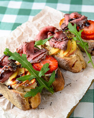 Italian Appetizer Bruschetta with roasted tomatoes, mozzarella cheese, garlic and herbs served over green tablecloth.