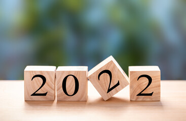 Wood blocks with number 2022 on wooden table over blur green tree background. Happy new year 2022