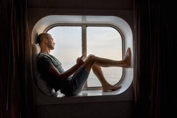Fototapeta na wymiar young man seated in front of a porthole reading a digital book