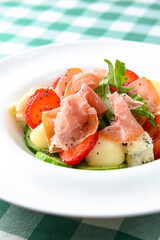 Salad with strawberry, prosciutto, herbs, cottage cheese and blackberry balsamic vinegar arranged on white plate.