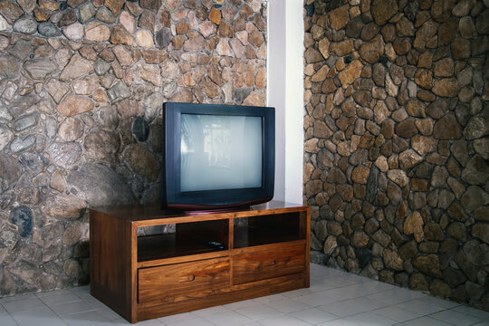 Old TV with empty screen on wooden table in living room with stone wall in the background.