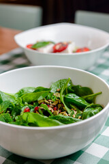Spinach salad with tomatoes, fresh arugula, pumpkin seeds, pomegranate seeds served in a white bowl