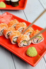 California sushi rolls served on a red plate over light wooden background. Close up, selective focus on sushi.