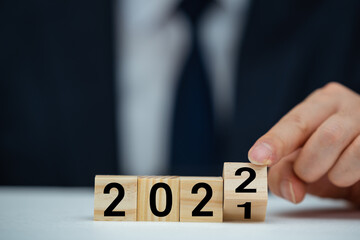 Businessman hand holding wooden cube with flip over block 2021 to 2022 text on table background.
