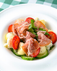 Salad with strawberry, prosciutto, herbs, cottage cheese and blackberry balsamic vinegar arranged on white plate.