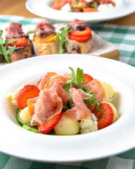 Salad with strawberry, prosciutto, herbs, cottage cheese and blackberry balsamic vinegar arranged on white plate.