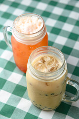 Row of fresh boba bubble tea glasses on wooden table with green plaid tablecloth background.