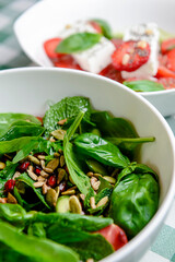 Spinach salad with tomatoes, fresh arugula, pumpkin seeds, pomegranate seeds served in a white bowl
