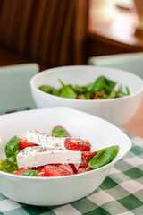 Caprese salad with strawberry, mozzarells, basil and balsamic sauce served in a white bowl over green plaid background.