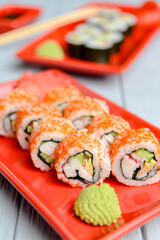California sushi rolls served on a red plate over light wooden background. Close up, selective focus on sushi.