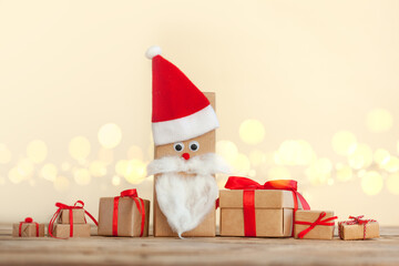 Obraz na płótnie Canvas Many Handmade Christmas boxes wrapped in craft gift paper decorated with Santa Hat on wooden background with sparkling bokeh.Secret Santa concept