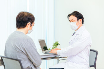 Fototapeta premium パソコンで診察するマスク姿の男性医師 