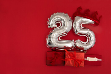 Foil silver air balloons showing number 25 twenty five placed on red background with wrapped...