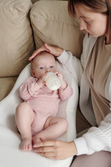 Adorable baby girl lying on small white soft bed and having milk from bottle