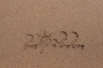 Summer vacation 2022 concept. Happy New Year 2022, lettering on the beach and clear sea. Numbers 2022 year on the sea shore, message handwritten in the golden sand. New Years concept.