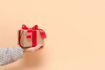 Hand hold gift box tied with red ribbon on a beige background. Festive concept with place for text.