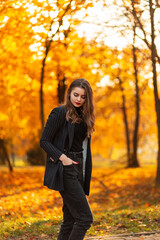 Young beautiful girl in a black stylish suit with a fashionable blazer on nature with bright autumn leaves at sunset