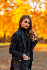 Fashionable portrait of a beautiful elegant woman with red lips in a stylish blazer with a sweater on the background of an amazing autumn park with yellow fall foliage