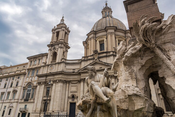 Obraz premium A statue of the the Ganges river god, part of the Fontana dei Quattro Fiumi (Fountain of the Four Rivers), with Sant'Agnese in Agone church in background, in the Piazza Navona, Rome, Italy 