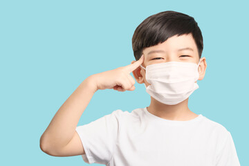 Portrait of a smart and healthy asian boy in white t-shirt with medical face mask pointing his head as he thinking and smile. Turquoise blue background, New normal, Back to school, Poster, Copy space.