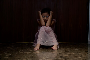 Sadness offended little girl scared. A Child sitting in a dark corridor in front of the door with light.