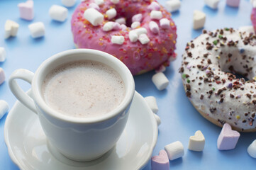 Pink and white donuts, cup of cocoa marshmallows in the shape of heart on blue background