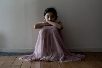 Fototapeta premium Sadness offended little girl scared. A Child sitting in a dark corridor in front of the door with light.