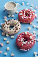 Pink and white donuts, cup of cocoa, marshmallows in the shape of heart on blue background