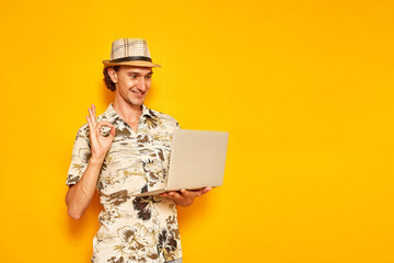 male tourist traveler on vacation with laptop in his hand shows OK sign, everything is fine via...