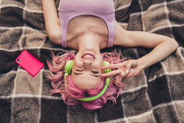 Naklejka premium Top above high angle photo of young girl happy positive smile lying blanket listen music earphones show peace v-sign outdoors