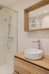 Modern bathroom with shower, round white sink, wooden base and mirror frame. Minimalist style interior design in warm colors.