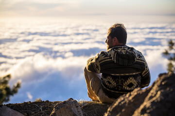 Back of man relaxing and admiring scenic cloudscape from mountain top. Hiker admiring stunning...