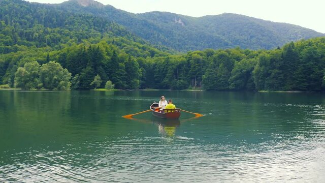Young couple are sailing on a old wooden boat in Biogradsko Lake in Montenegro. Aerial view 4K.