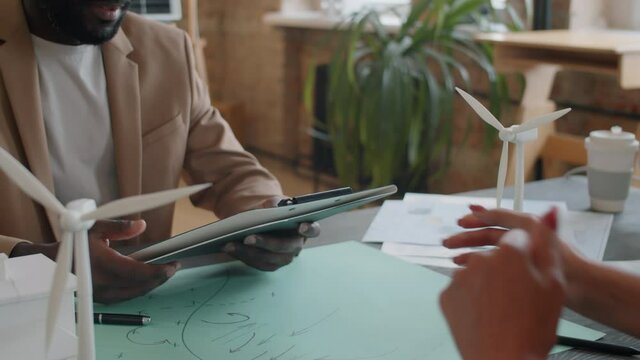 Close up shot of Afro-American businessman taking contract from Caucasian female colleague and giving her handshake at office table with windmill turbines models on it