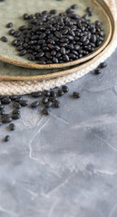 Fototapeta na wymiar Ceramic plate full of dry black beans on grey table closeup