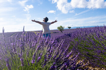 Carefree male tourist standing with his arms wide outstretched amidst lavender flower agricultural field against cloudy sky. Man enjoying his freedom in beautiful lavender flower field