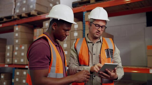 Male colleagues checking deliveries for new packages on digital tablet standing in factory 